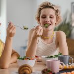 Two women enjoying a healthy meal at a cozy dining table, sharing a joyful indoor breakfast moment.